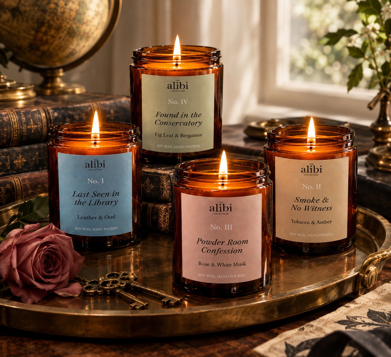 All four Alibi Collection candles lit together on a brass tray, with old books, a globe and a rose